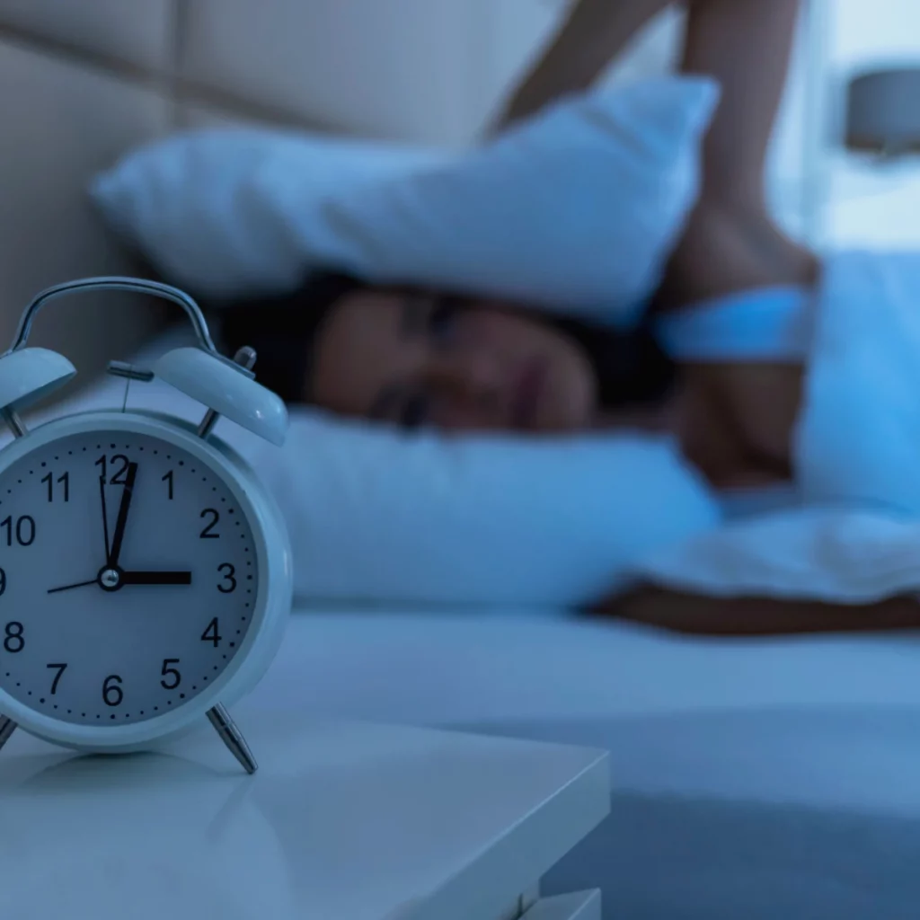 Réveil affichant 3h du matin près d'une personne qui se réveille dans la nuit