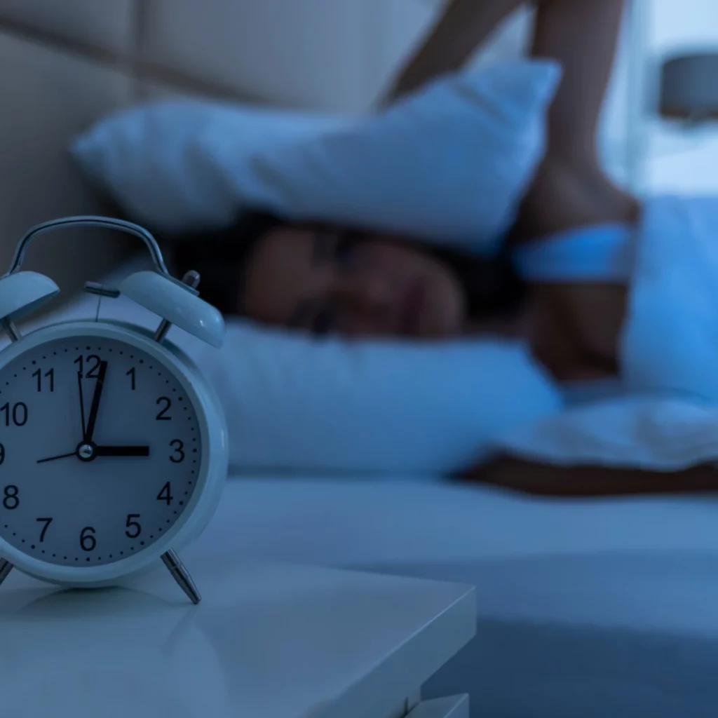 Réveil affichant 3h du matin près d'une personne qui se réveille dans la nuit